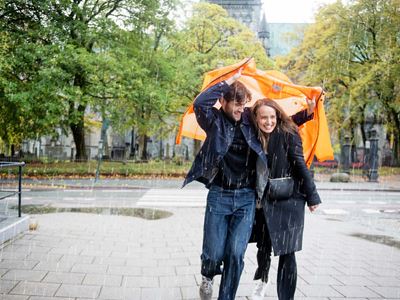 Ungt par løper i regnet med en oransje jakke over seg